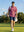 Model in rose flower performance jersey print polo with a golf bag over shoulder outdoors, full-body shot