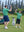 Adult and child models in green stripe performance cooling polo high-fiving outdoors.