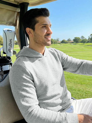 A man wearing a light grey heather textured solid hoodie pullover, sitting in a golf cart 