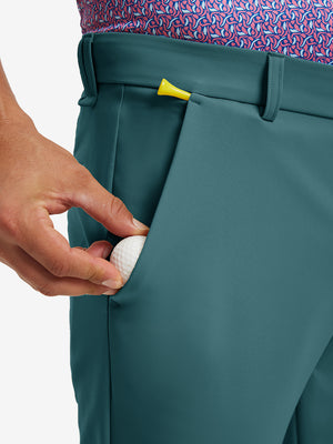 Hand placing a golf ball into pocket of water-resistant golf stretch nylon pants in dark teal.