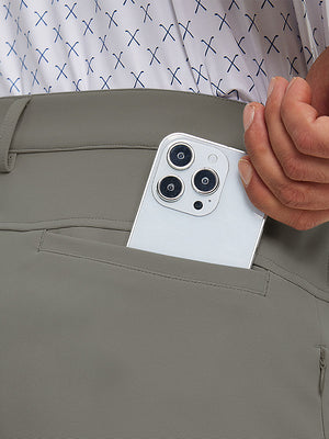 Close detail of hand placing phone into back pocket of lightweight moisture wicking dress pants in dark khaki.