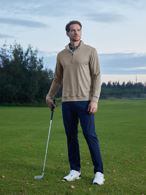 Model on grass under blue sky, leaning on golf club, wearing quarter zip melange pullover in brown melange.