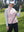 Model leaning on a golf cart, wearing light pink women's lightweight slim-fit puffer vest with one hand in pocket.
