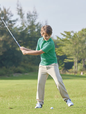 The model is wearing Boys Stretch Fleece Lined Casual Golf Pants in LIGHT KHAKI while playing golf on the golf course.