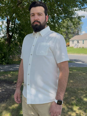 Model standing on grass with trees and house behind, wearing traditional breathable solid shirt in beige