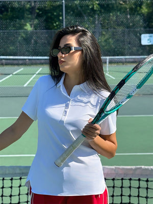 Model in white women's performance solid polo holding a badminton racket outdoors, waist-up shot